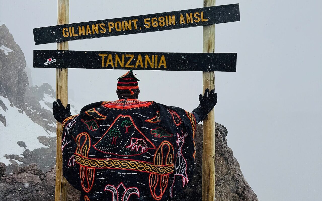 Rear view of Afowiri Fondzenyuy wearing traditional Toghu attire from Cameroon at Gilman’s Point (5,681 m) on Mount Kili